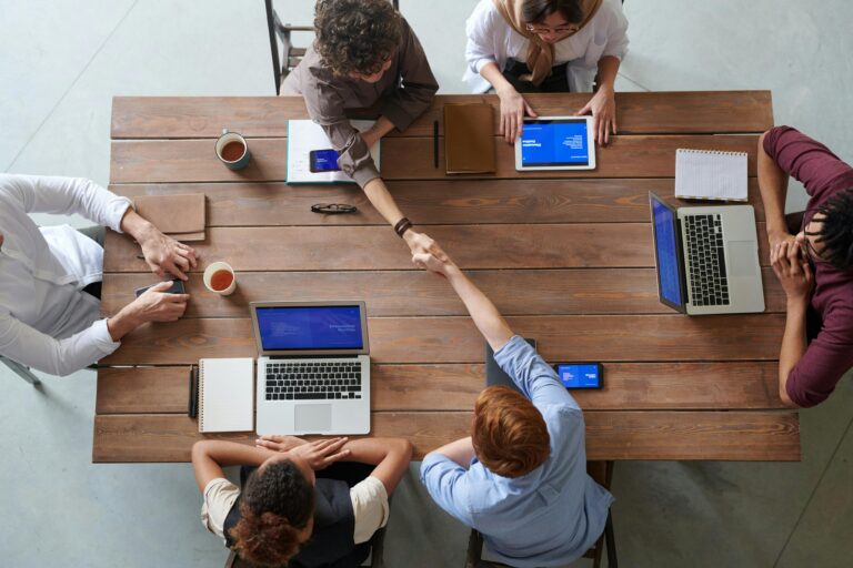Teammeeting mit Laptops und Handschlag – Symbol für Zusammenarbeit und Abstimmung.