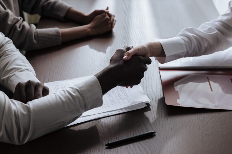 "Handschlag über Bewerbungsunterlagen am Schreibtisch als Symbol für erfolgreichen Recruiting-Abschluss
